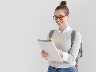 Indoor shot of young European female on right side of photo against gray background taking notes on...