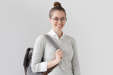 Photo of young European female isolated on grey background, wearing grey trendy backpack and...
