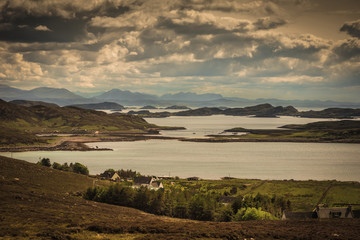 Assynt Peninsula, Scotland - June 7, 2012: Altandhu hamlet on Atlantic Ocean inlet shore with multitude of rocky islets under heavy storm sky. Mountain peaks in background.
