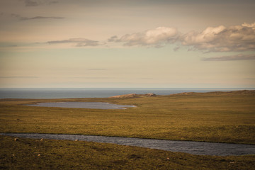 Assynt Peninsula, Scotland - June 7, 2012: Flat land with dry vegetation and cut by creek and lake descends to Atlantic Ocean. Twilight sky with white clouds at Brae of Achnahaird. Total desolation.