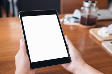 Mockup image of hands holding black tablet pc with white blank screen on wooden table background in coffee shop