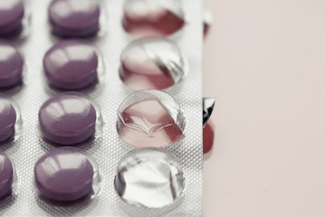 Close-up of purple pills in a pack on a pink background.