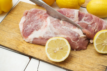 Frozen piece of meat andyellow lemon on a wooden cutting board