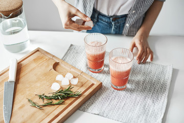 Obraz na płótnie Canvas Close up of girl's hands putting ice pieces in glasses with grapefruit detox healthy smoothie.
