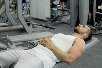 Muscular tired man lies on a bench after exercise in the gym
