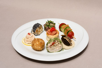 Different types of canapes, placed on white plates, finger food, light brown background