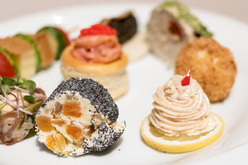 Different types of canapes, placed on white plates, finger food, light brown background