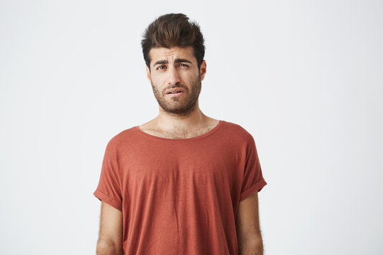 Bearded stylish male having displeased look standing in casual cloth against white background. Young man having some problems looking with unsatisfaction and discontent into camera.