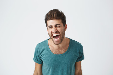 Obraz premium Indoor shot of furious young good-looking European man in casual cloth screaming with anger and rage, keeping his eyes closed. Student having an argument with his girlfriend. Human face expressions