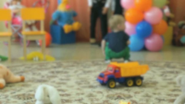 Unrecognizable person, blurred video. Little child aged 5s sits on the carpet in the hall of the kindergarten