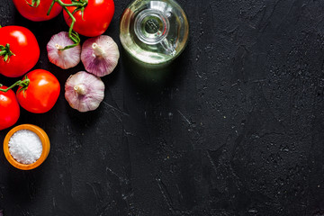 Cook workplace. Tomato, garlic, oil, salt on black table background top view copyspace