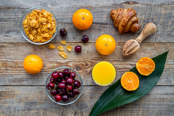 Obraz na płótnie Canvas Light summer breakfast. Muesli, oranges, cherry and croissant on wooden table background top view