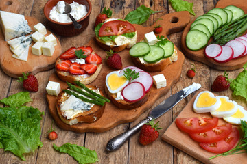 Set of healthy whole wheat bread sandwiches with fuits, vegetables, cheese and leafy green herbs on picnic wooden table. Ciabatta sandwich bar or buffet. Top view. Making lunch time snacks concept