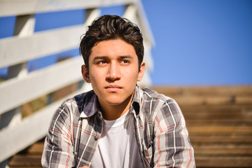 Attractive young male, sitting on steps outdoors, looking off into the distance, thinking
