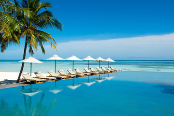 Large infinity pool on the shores of the Indian Ocean with sunbeds and umbrellas in the shade of the palm trees