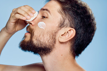 Young guy with a beard on a blue background, cream, cotton ball