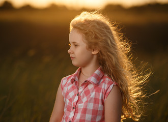 Little blonde child girl standing in summer field at sunset.
