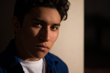 Handsome and attractive hispanic teenager, partially in shadows, looking at camera