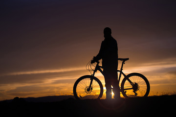 A guy with a bicycle on a sunset background. Silhouette.