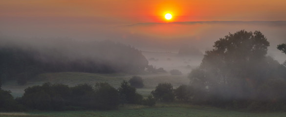 Foggy summer morning over the valley, fog and rising sun