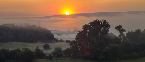 Obraz premium Foggy summer morning over the valley, fog and rising sun
