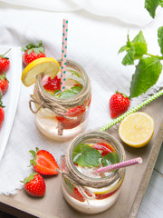 Mineral  water with fresh strawberries, lemon  and mint in jar on a white wooden background, copy space