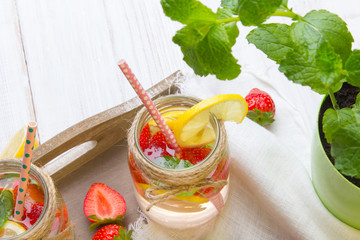 Mineral  water with fresh strawberries, lemon  and mint in jar on a white wooden background, copy space