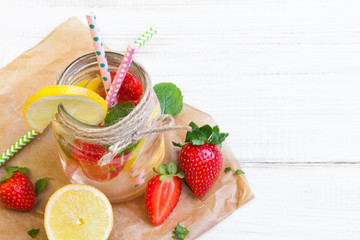Mineral  water with fresh strawberries, lemon  and mint in jar on a white wooden background, copy space