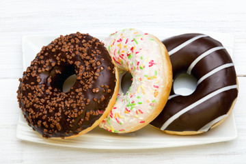 Tasty donuts with icing and chocolate on white wooden background, copy space