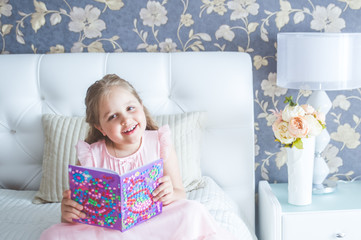 Little girl is sitting on the bed and reading a book