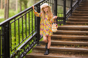 Sweet beautiful fashionable girl in a hat and a bag up the stairs in the park.