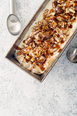 Snickers ice cream with caramel,  fried peanuts and hazelnuts in metallic baking tray on rustic background. Gourmet summer treat concept. Composition with copy space.