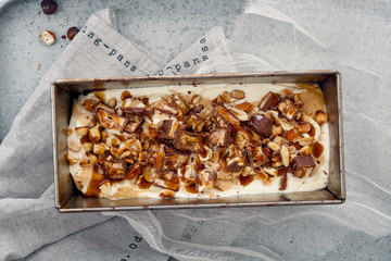Snickers ice cream with caramel,  fried peanuts and hazelnuts in metallic baking tray on rustic background. Gourmet summer treat concept. Composition with copy space.