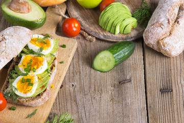 Avocado and egg sandwich on a wooden background. Fresh organic vegetables, eggs and whole wheat bread. Healthy breakfast. Rustic style.