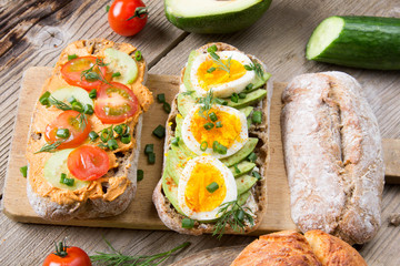 Sandwiches with avocado, eggs and tomato on a wooden background. Fresh organic vegetables, eggs and whole wheat bread. Healthy breakfast. Retro style.