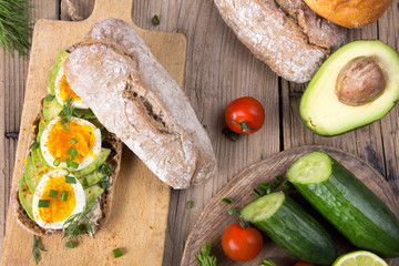 Avocado and egg sandwich on a wooden background. Fresh organic vegetables, eggs and whole wheat bread. Healthy breakfast. Rustic style.