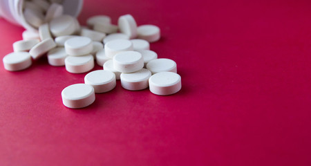 Many pills poured from the vial on red background.