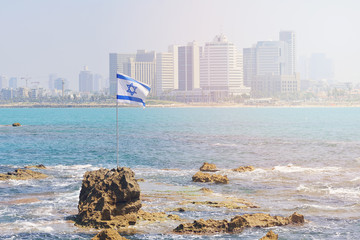 The flag of Israel against the background of modern Tel Aviv, the Mediterranean Sea.