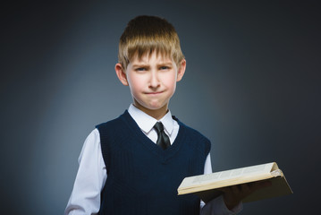 Handsome little stressed boy with book isolated on gray background