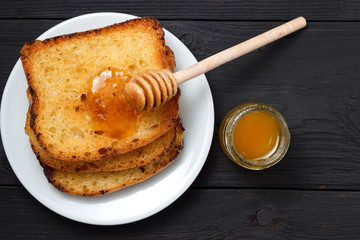 Three toasted toasts on a white plate with honey and a honey spoon