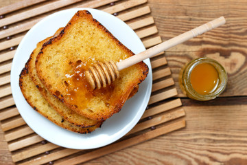 Fried toast on a white plate with a jar of honey and a spoon on a wooden background