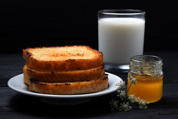 Toast on a plate with milk and a can of honey. On a black wooden background