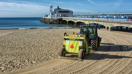A tractor cleans the sand by raking it and picking up debri on the beach  at the english seaside...