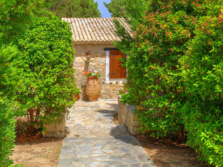 View on family Greece traditional Greek village style hotel entrance green gate, antique classical vase jar flowers. Gingerbread Classic Greece architecture Greece holidays vacations sightseeing tours