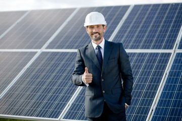 Happy business client showing thumb up. Man in suit and white helmet standing smiling, choosing solar energy.