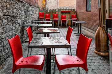 Wet tables outside restaurant by sidewalk with cobblestone European street during heavy rain