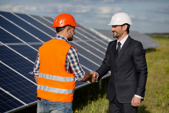 Businessman and foreman shaking hands at solar energy station. Solar panels in the field, two men making agreement.
