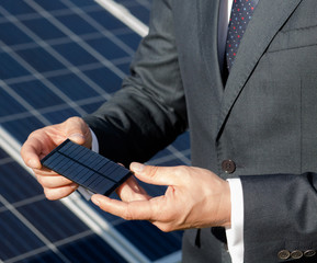 Businessman holding photovoltaic element in his hands. Close up view on photovoltaic detail of solar panel in mans hands.