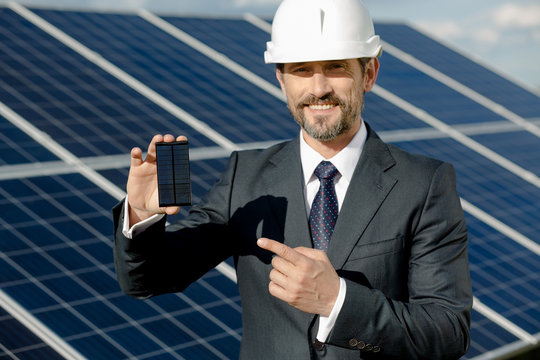 Business client showing photovoltaic detail of solar panel. Man in business suit and white helmet at solar energy station.