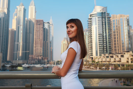 Happy beautiful tourist woman in fashionable summer white dress walking and enjoying in Dubai marina in United Arab Emirates. Luxury and comfortable tourism season in UAE. Warm summer day.